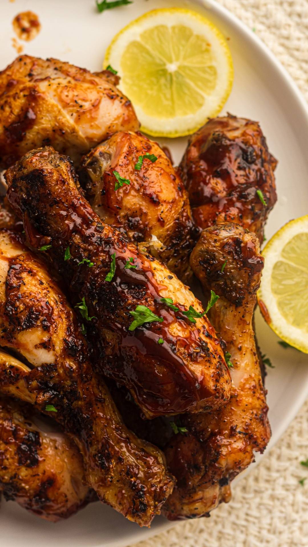 Plate of easy grilled chicken drumsticks glazed and seasoned, garnished with chopped herbs and served with lemon slices on a white plate.