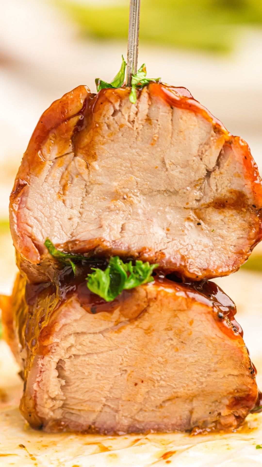 Two slices of grilled pork tenderloin stacked, topped with fresh herbs and drizzled with savory sauce, with a skewer inserted through the top.