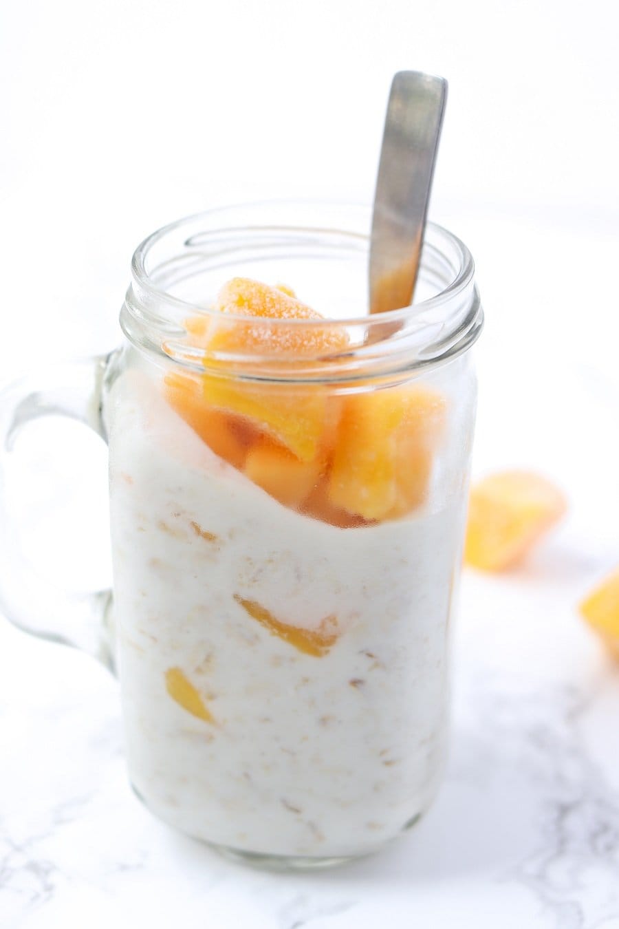 A mason jar filled with chia-free overnight oats and topped with mango chunks, with a spoon inside the jar.