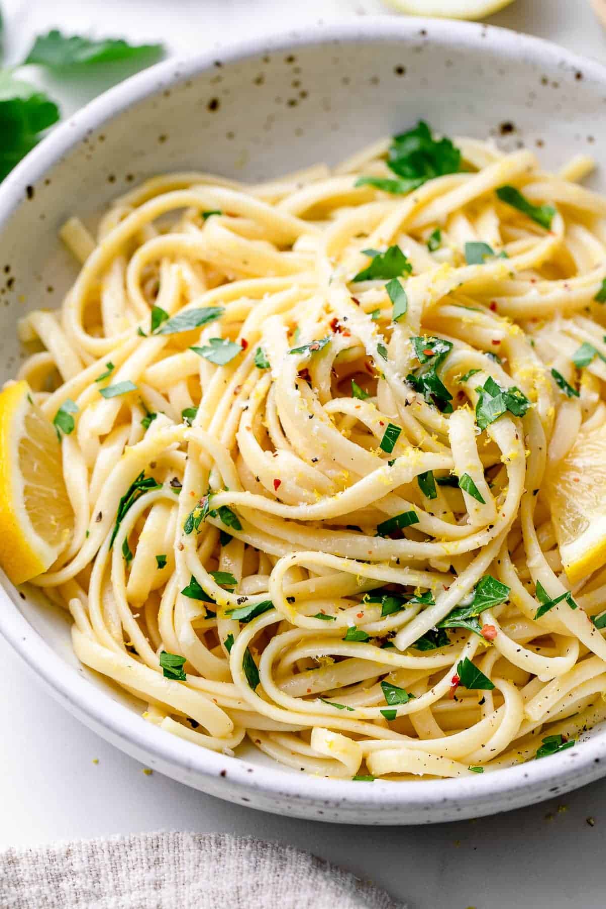 A bowl of linguine pasta garnished with chopped parsley, black pepper, red pepper flakes, and lemon wedges—perfect for those seeking fresh spring pasta recipes.