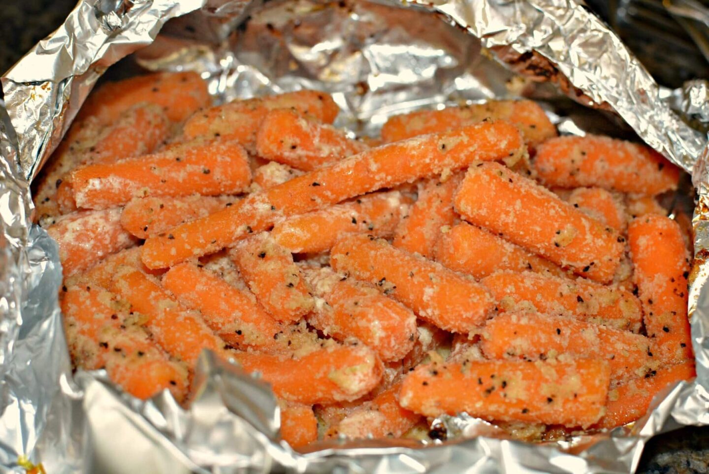 Baby carrots coated with seasoning and grated cheese, arranged on a sheet of aluminum foil, make a tasty addition to summer vegetable side dishes, ready for cooking or baking.