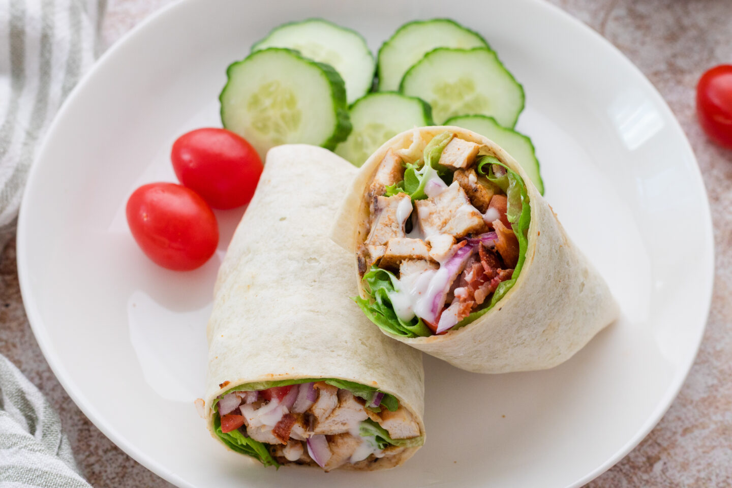 A plate with a sliced chicken wrap, lettuce, and vegetables, served with cucumber slices and cherry tomatoes—perfect for Summer Meals and easy Dinner Ideas.