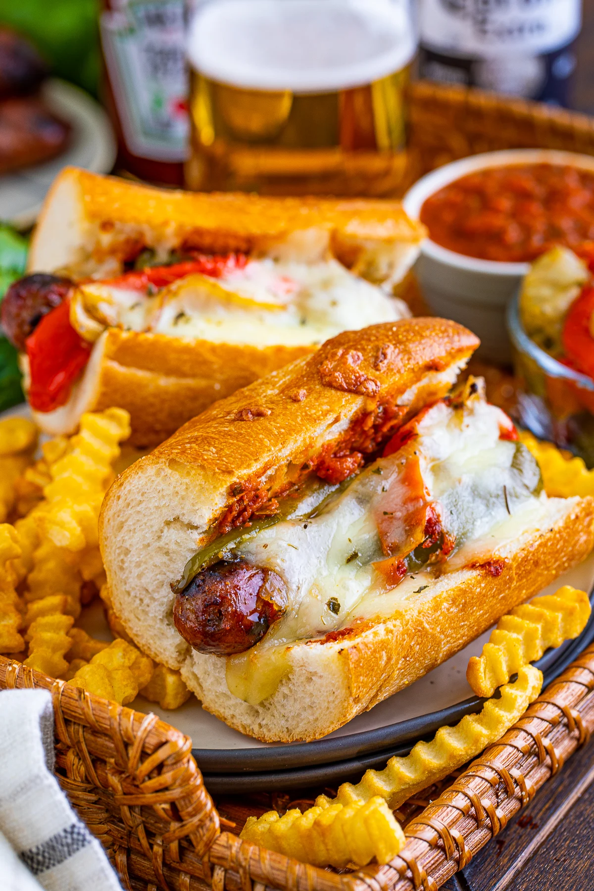 Two sausage hoagies with melted cheese and marinara sauce are served on a plate with crinkle-cut fries, making for perfect beach dinner ideas. Drinks and dipping sauces complete this mouthwatering meal.