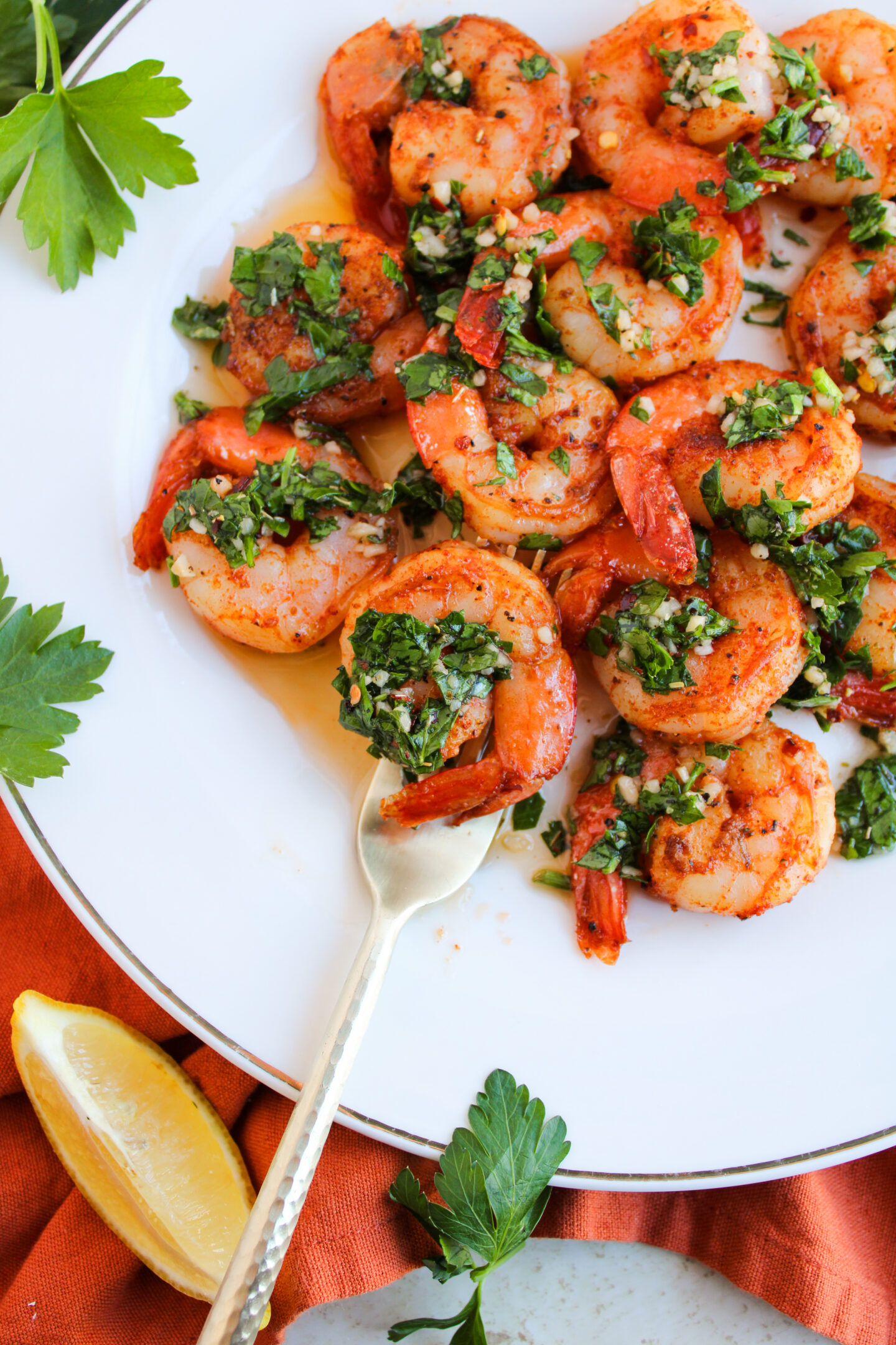 Cooked shrimp garnished with chopped herbs and sauce on a white plate, with a fork, parsley leaves, and a lemon wedge nearby—perfect for Father's Day dinner or new dinner ideas.