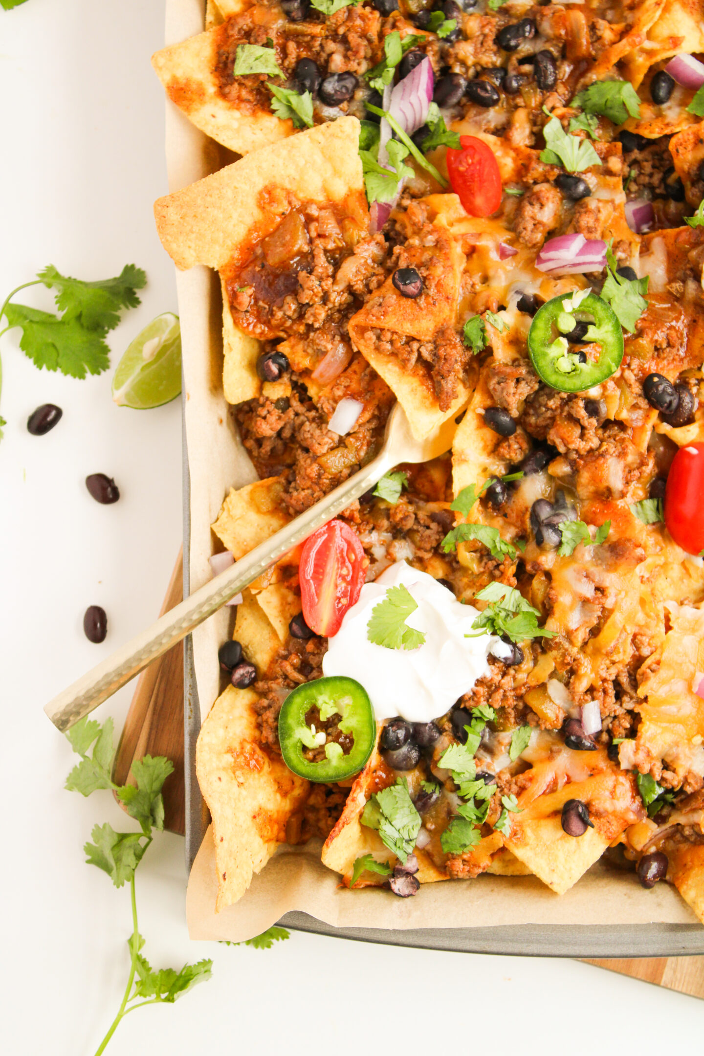 A tray of loaded nachos topped with ground meat, black beans, melted cheese, jalapeño slices, cherry tomatoes, red onion, sour cream, and cilantro—a perfect beach dinner for your next sunset gathering.