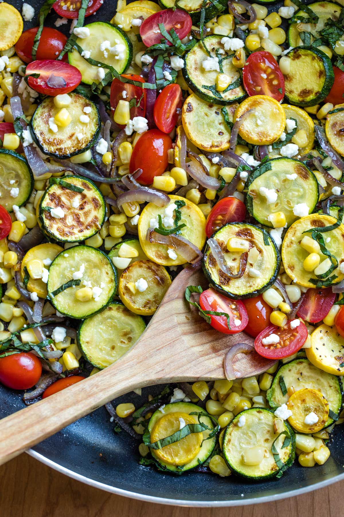 Sautéed zucchini, yellow squash, corn, cherry tomatoes, red onion, and crumbled cheese in a skillet—an easy favorite among summer vegetable side dishes.