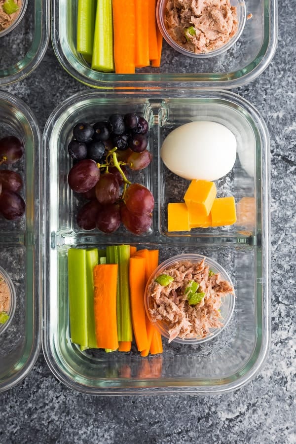 Glass meal prep container perfect for sports dinners, featuring sections of carrot and celery sticks, grapes, a hard-boiled egg, cheese cubes, and a portion of tuna salad.