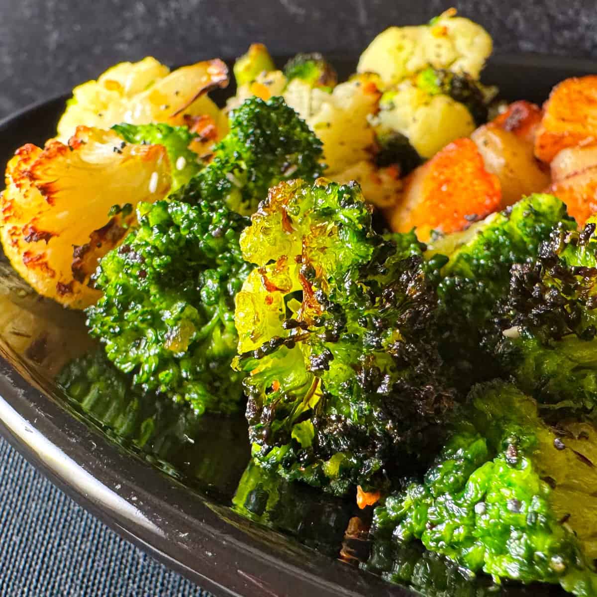 Close-up of roasted broccoli and cauliflower florets on a black plate, with visible seasoning and charred edges—perfect for summer vegetable side dishes.