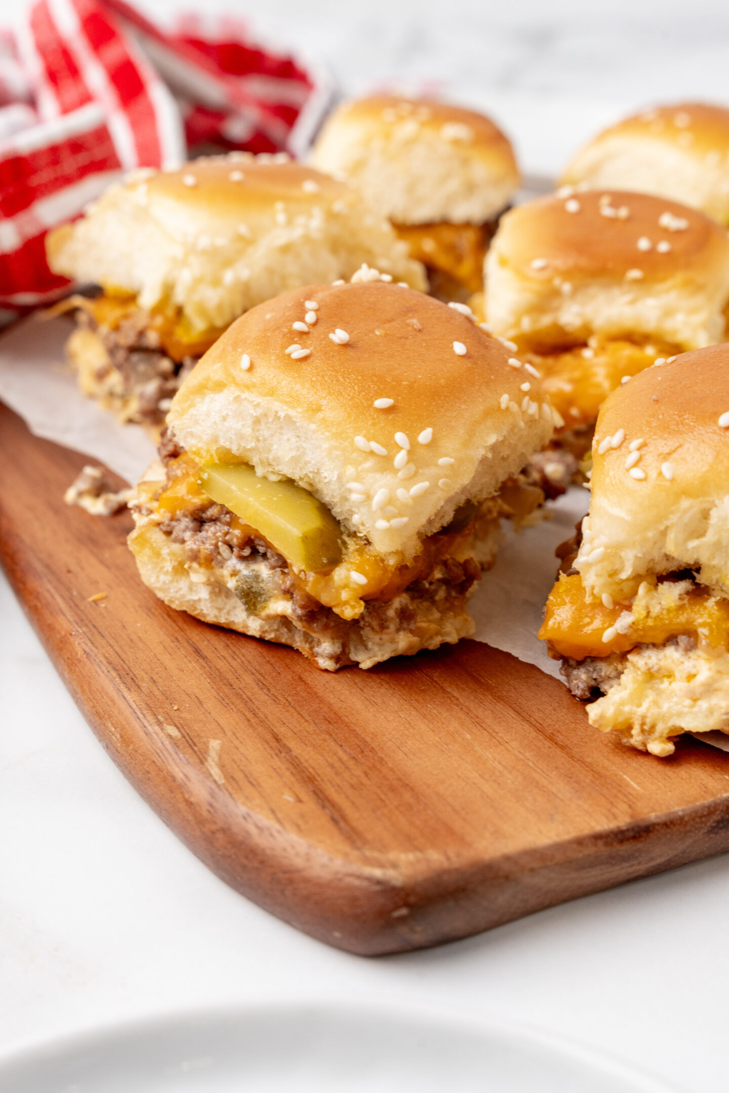 Several cheeseburger sliders with pickles and sesame seed buns are arranged on a wooden serving board, making them perfect for casual dinner ideas or a laid-back beach dinner.