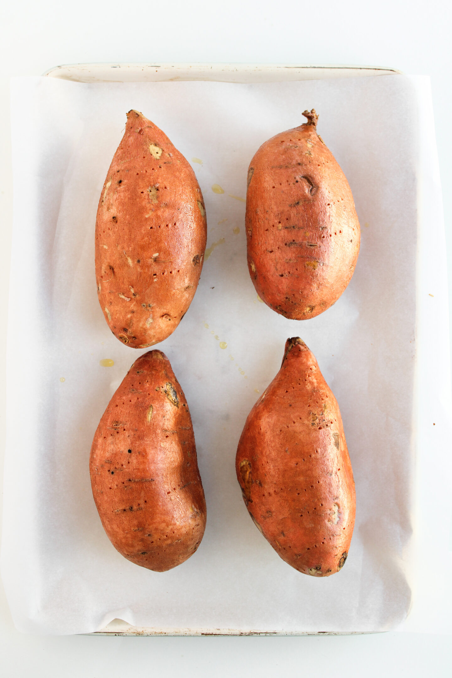 Four whole sweet potatoes placed on a parchment-lined baking sheet, spaced evenly apart—perfect for creating loaded sweet potatoes or experimenting with new sweet potato recipes.