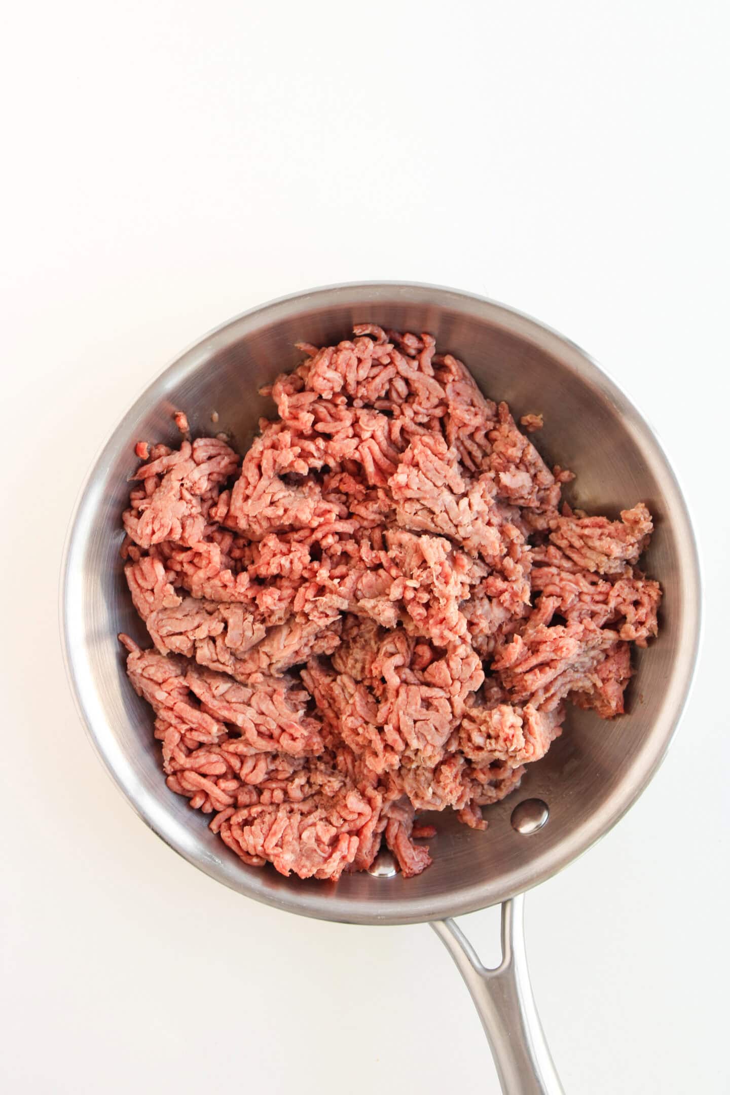 Raw ground beef in a stainless steel frying pan on a white background, perfect for crafting savory cheeseburger fillings or topping loaded sweet potatoes.
