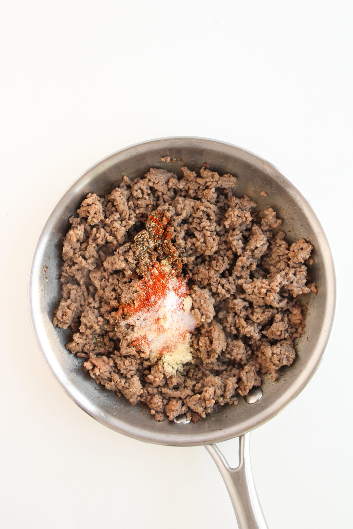 Cooked ground beef in a skillet with paprika, black pepper, garlic powder, and onion powder—perfect for topping loaded sweet potatoes or enjoying as a cheeseburger filling.