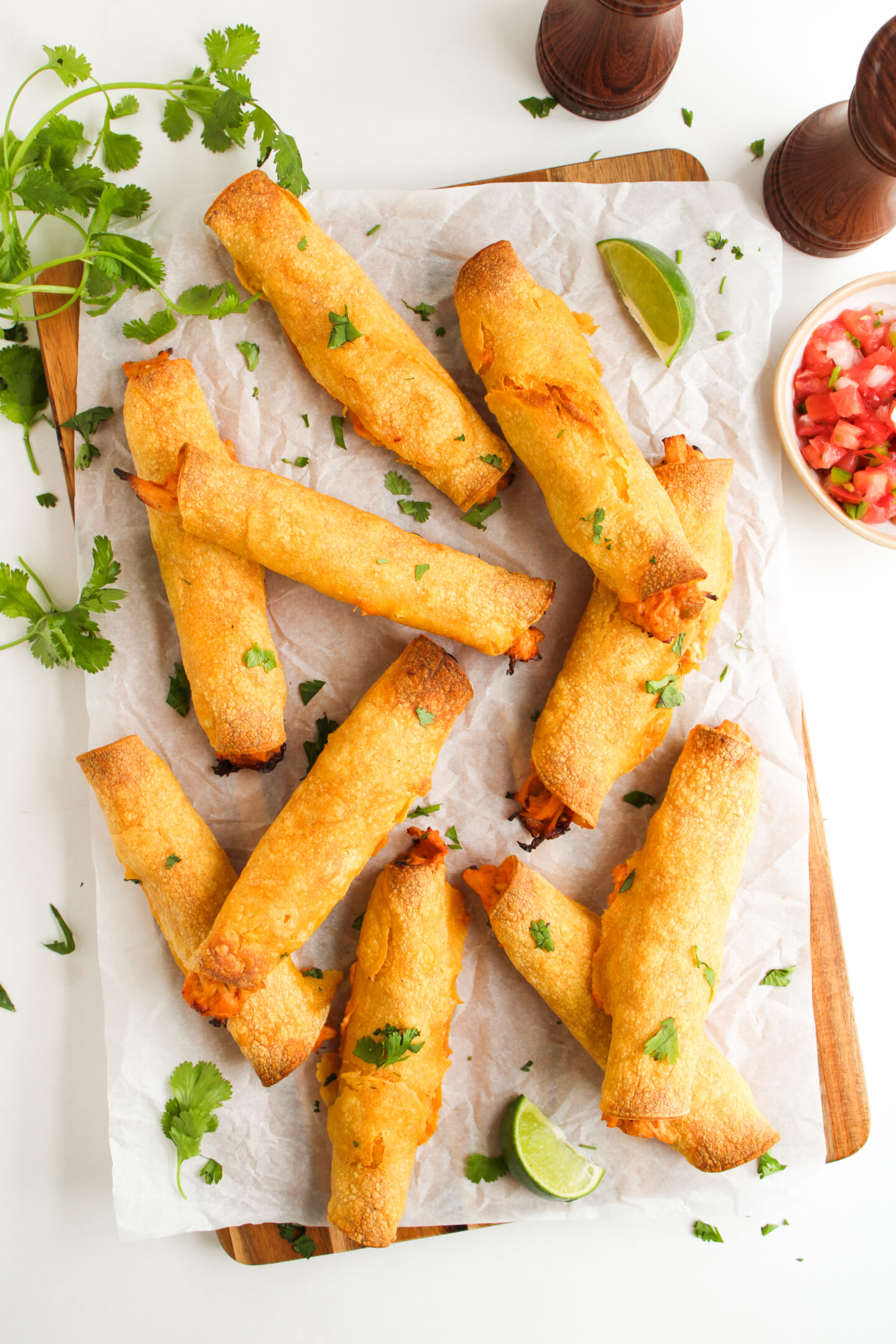 Seven baked taquitos garnished with chopped cilantro on parchment paper, with lime wedges, fresh cilantro, and a bowl of salsa on the side—perfect for summer dinner or easy June recipes.