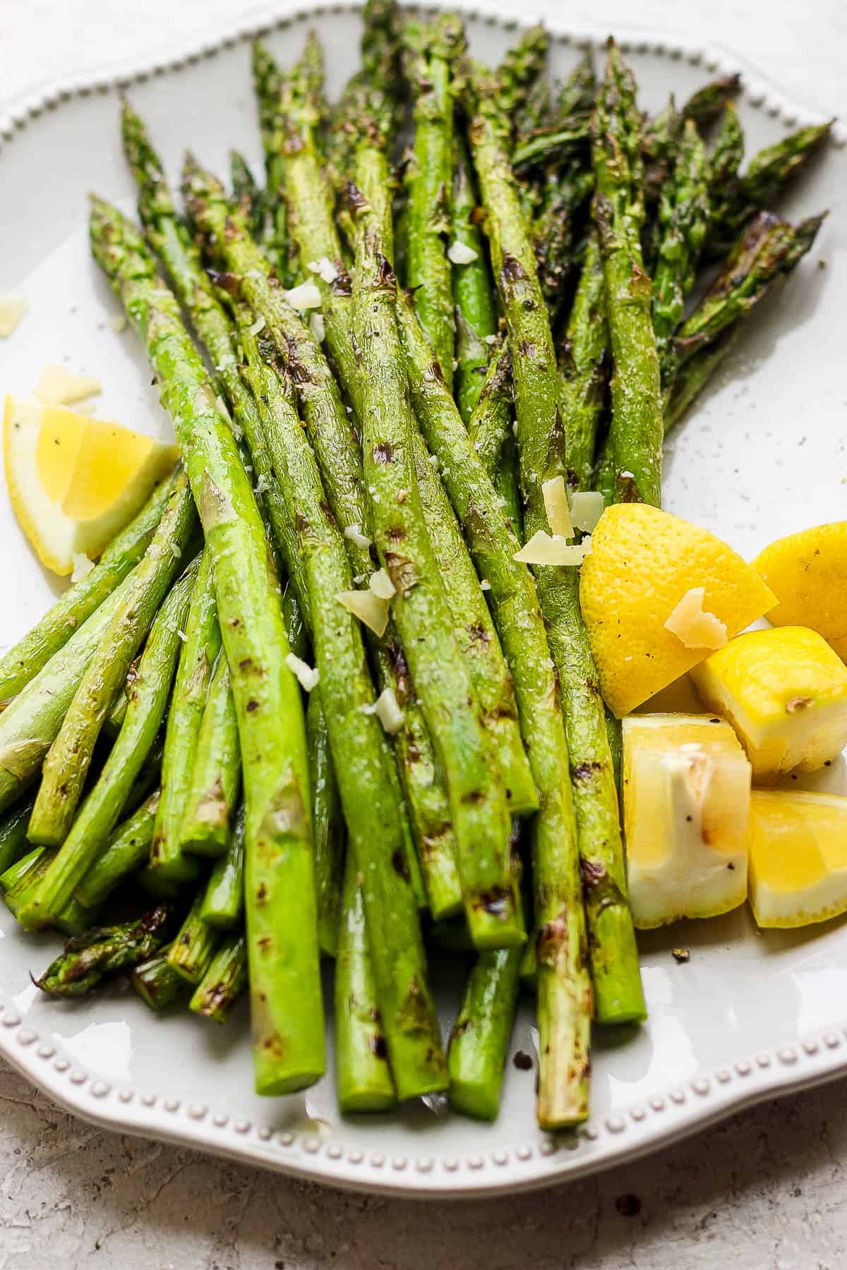 Grilled asparagus spears served on a white plate with lemon wedges and sprinkled with chopped garlic—an ideal choice for summer vegetable side dishes.