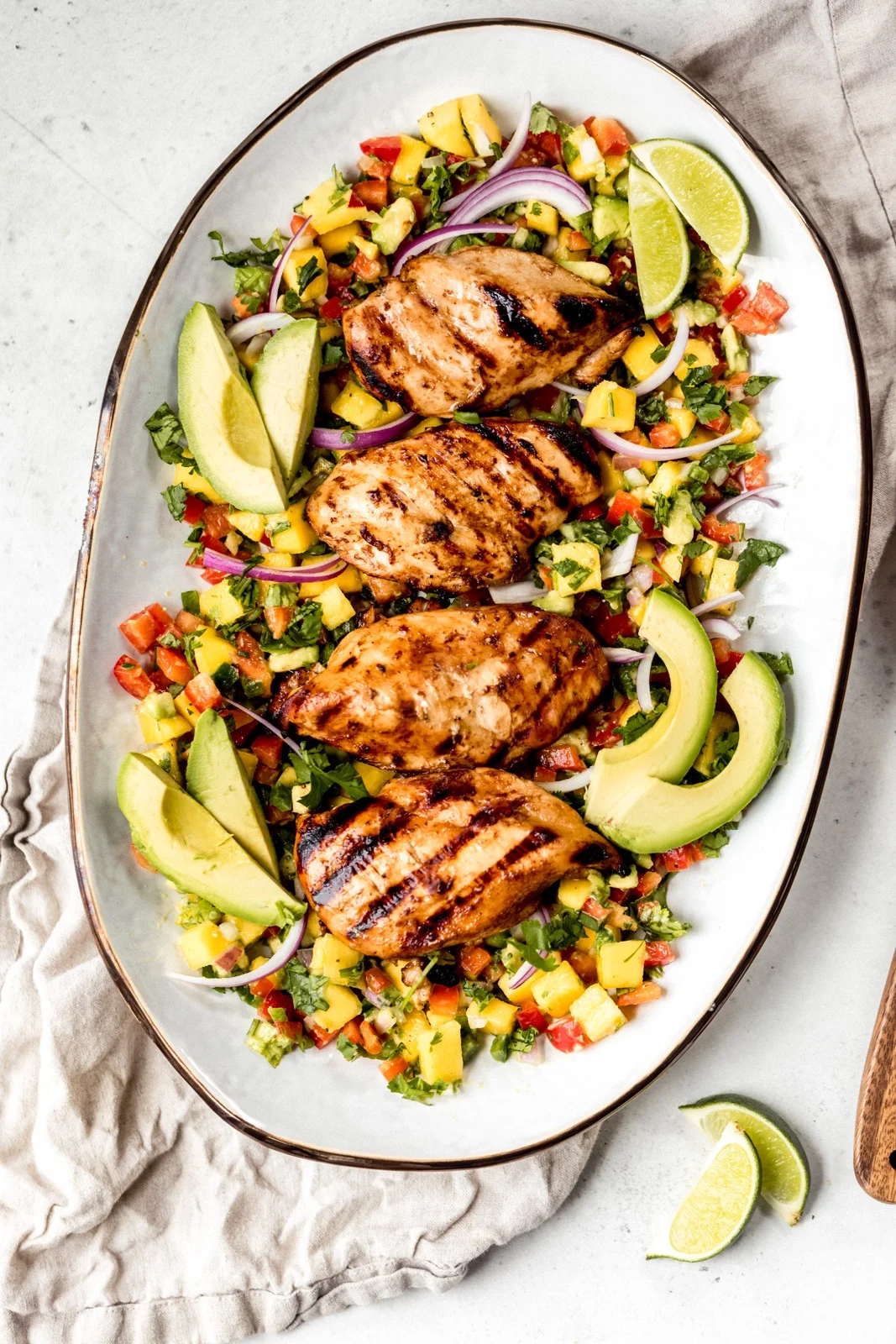 Grilled chicken breasts served on a platter with sliced avocado, red onion, lime wedges, and a colorful chopped vegetable salsa—perfect for relaxed beach dinner vibes and easy dinner ideas.