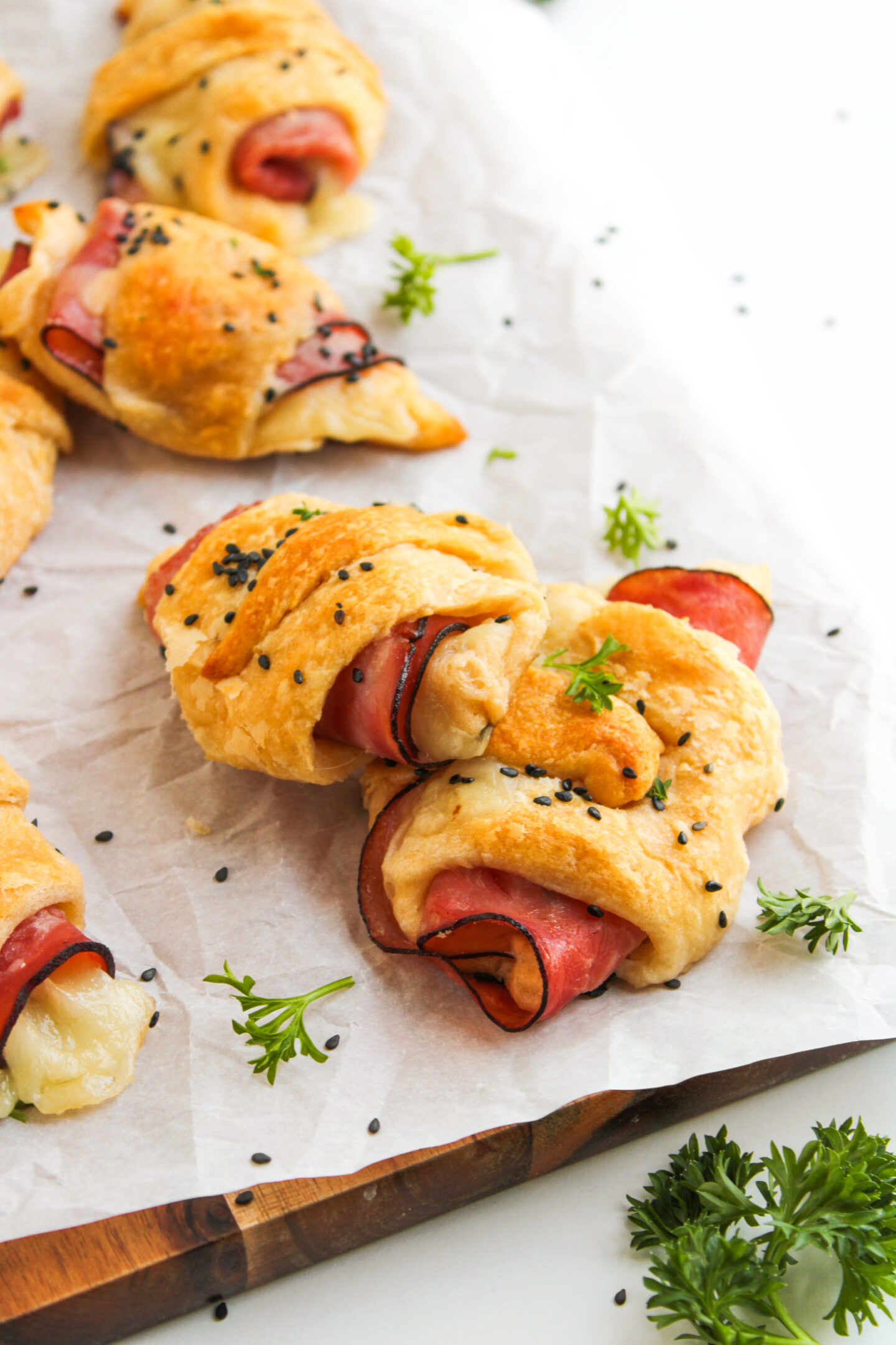 Crescent rolls filled with ham and cheese, topped with black sesame seeds and parsley—perfect for easy Sports Dinners, arranged on parchment paper for a crowd-pleasing bite.