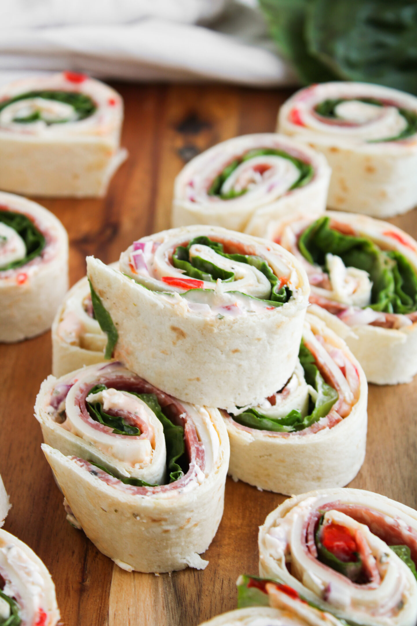 A close-up of tortilla pinwheel sandwiches filled with deli meat, cheese, lettuce, and other ingredients, perfect for Sports Dinners and arranged beautifully on a wooden surface.