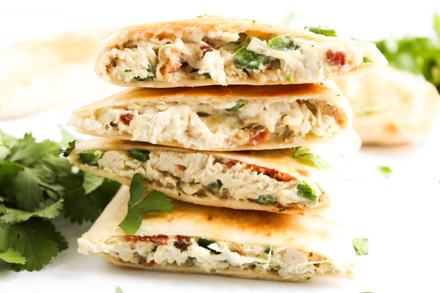 Four halved quesadillas stacked on top of each other, filled with shredded chicken, herbs, and small pieces of vegetables—perfect for Sports Dinners—with fresh cilantro leaves in the background.