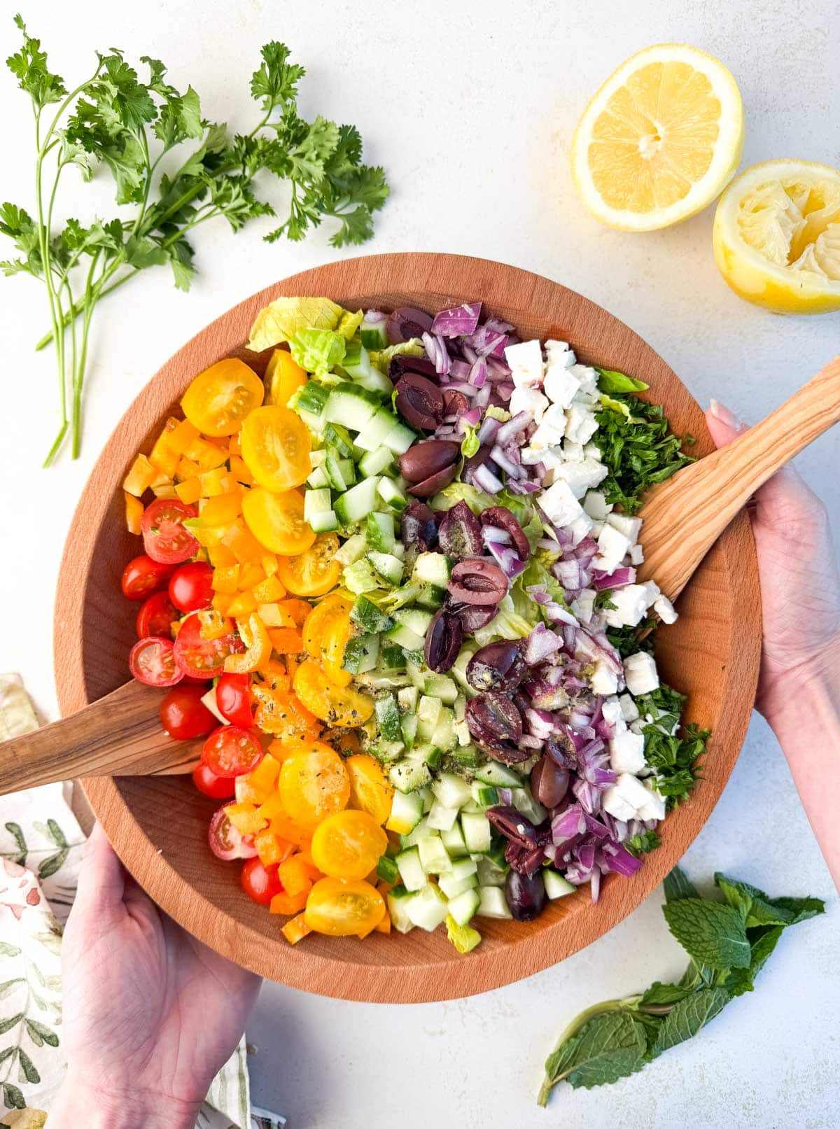 A wooden bowl filled with a colorful chopped salad featuring tomatoes, cucumbers, red onion, olives, and feta cheese sits on the table—perfect for those seeking fresh Summer Vegetable Side Dishes.