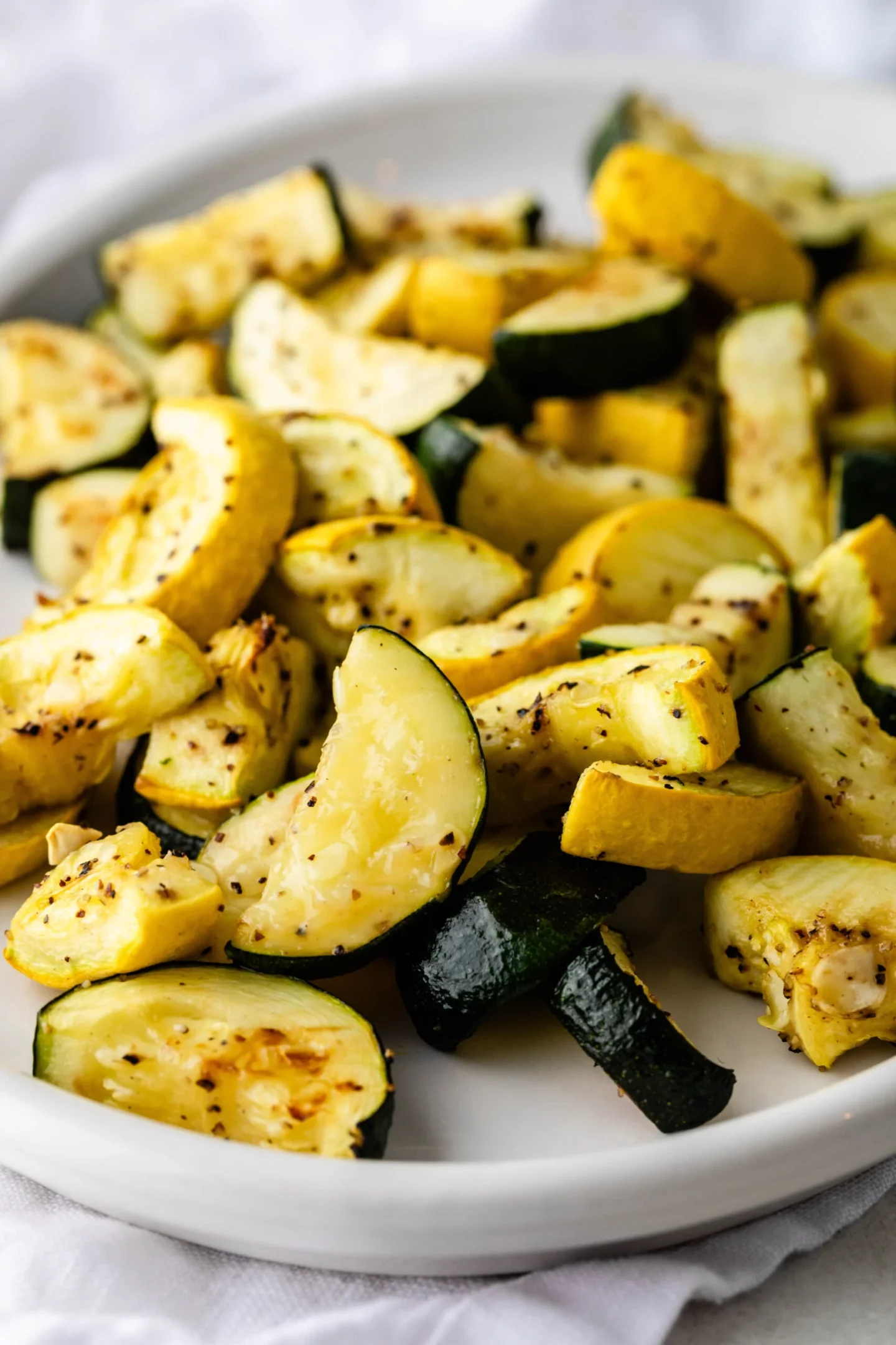 A white plate filled with roasted zucchini and yellow squash pieces, seasoned with herbs and pepper—a vibrant addition to your summer vegetable side dishes.