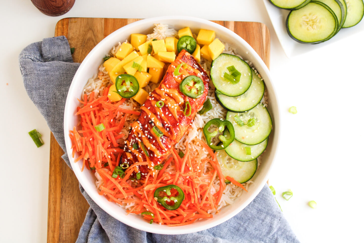 A bowl of rice topped with glazed salmon, shredded carrots, mango cubes, cucumber slices, jalapeño slices, sesame seeds, and green onions—perfect for Father's Day Dinner or fresh dinner ideas to celebrate.