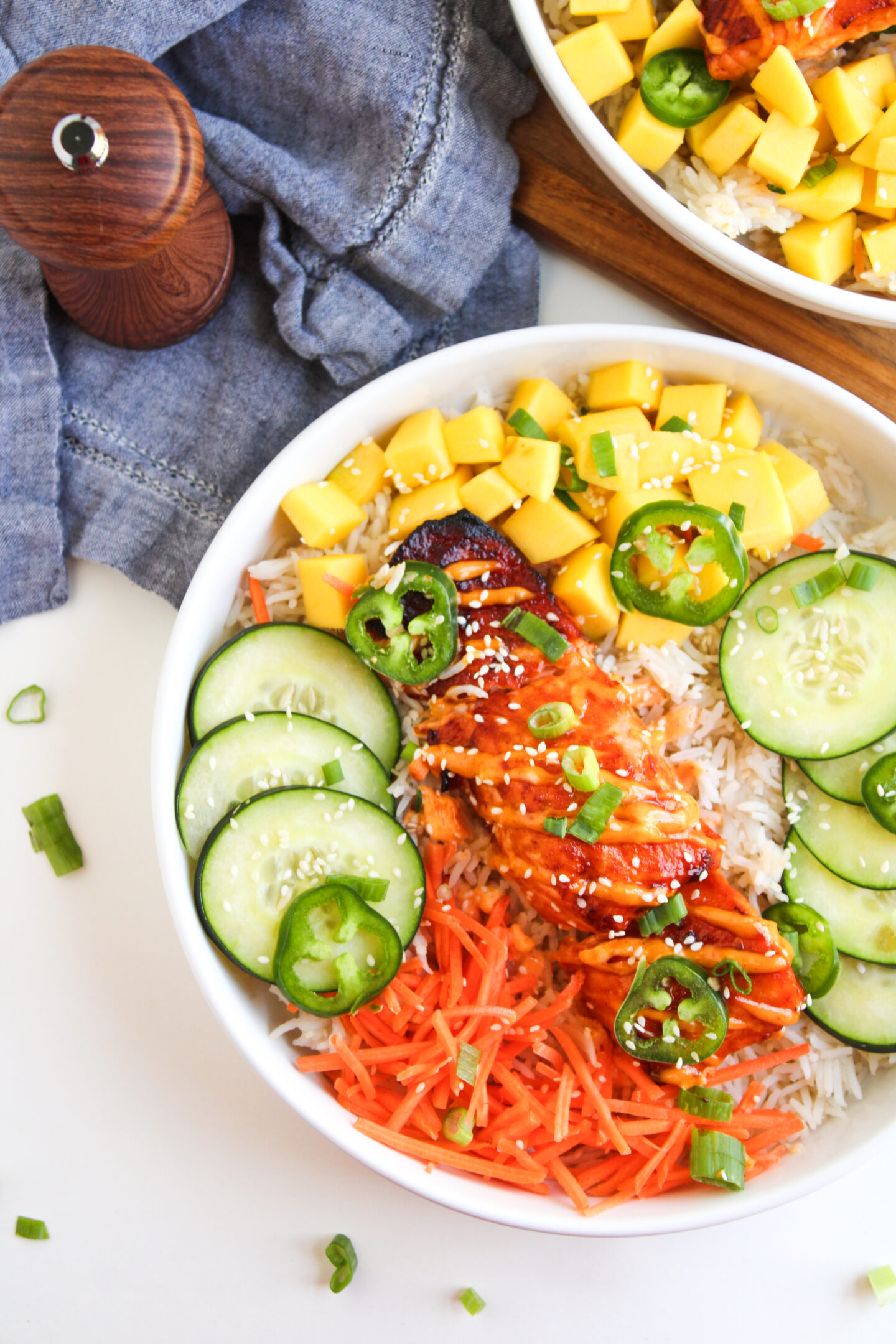 A bowl of rice topped with sliced cucumbers, shredded carrots, diced mango, grilled chicken, jalapeño slices, sesame seeds, and chopped green onions—perfect for fresh dinner ideas or as a tasty beach dinner.