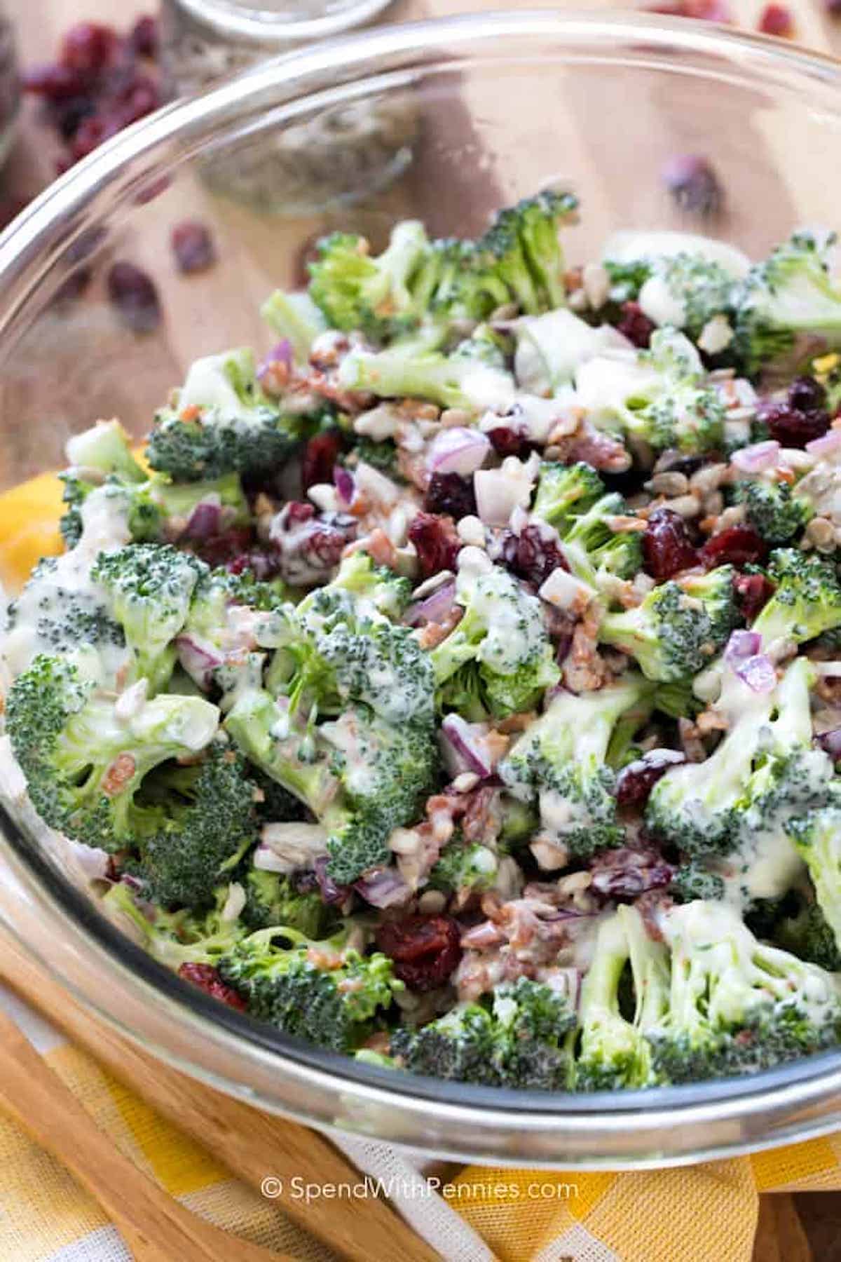 A glass bowl filled with broccoli salad, featuring chopped broccoli, red onions, dried cranberries, sunflower seeds, and a creamy dressing—perfect as one of the side dishes for your graduation party.