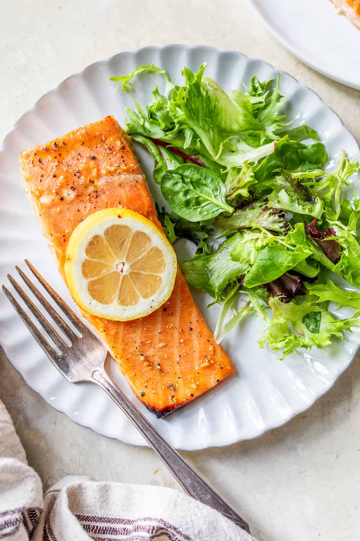 A plate with a baked salmon fillet topped with a lemon slice, served alongside a mixed green salad and a fork—perfect for those seeking healthy grilled dinners.