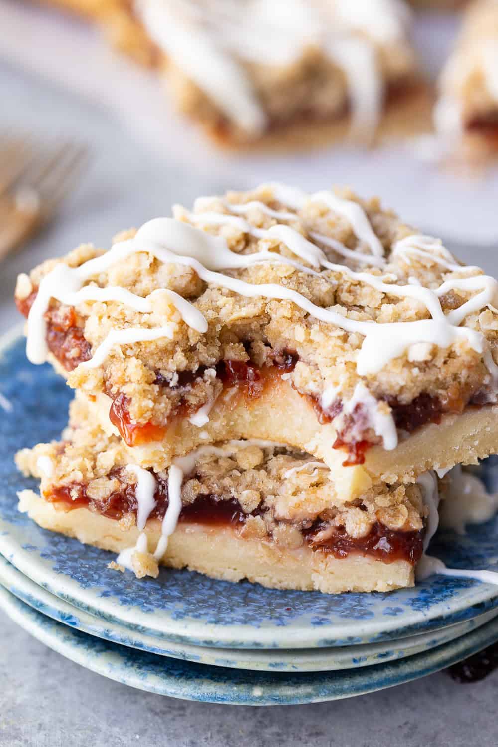 Two stacked cherry crumb bars with a fruit filling and white icing drizzle, served on blue patterned plates—a perfect summer dessert.