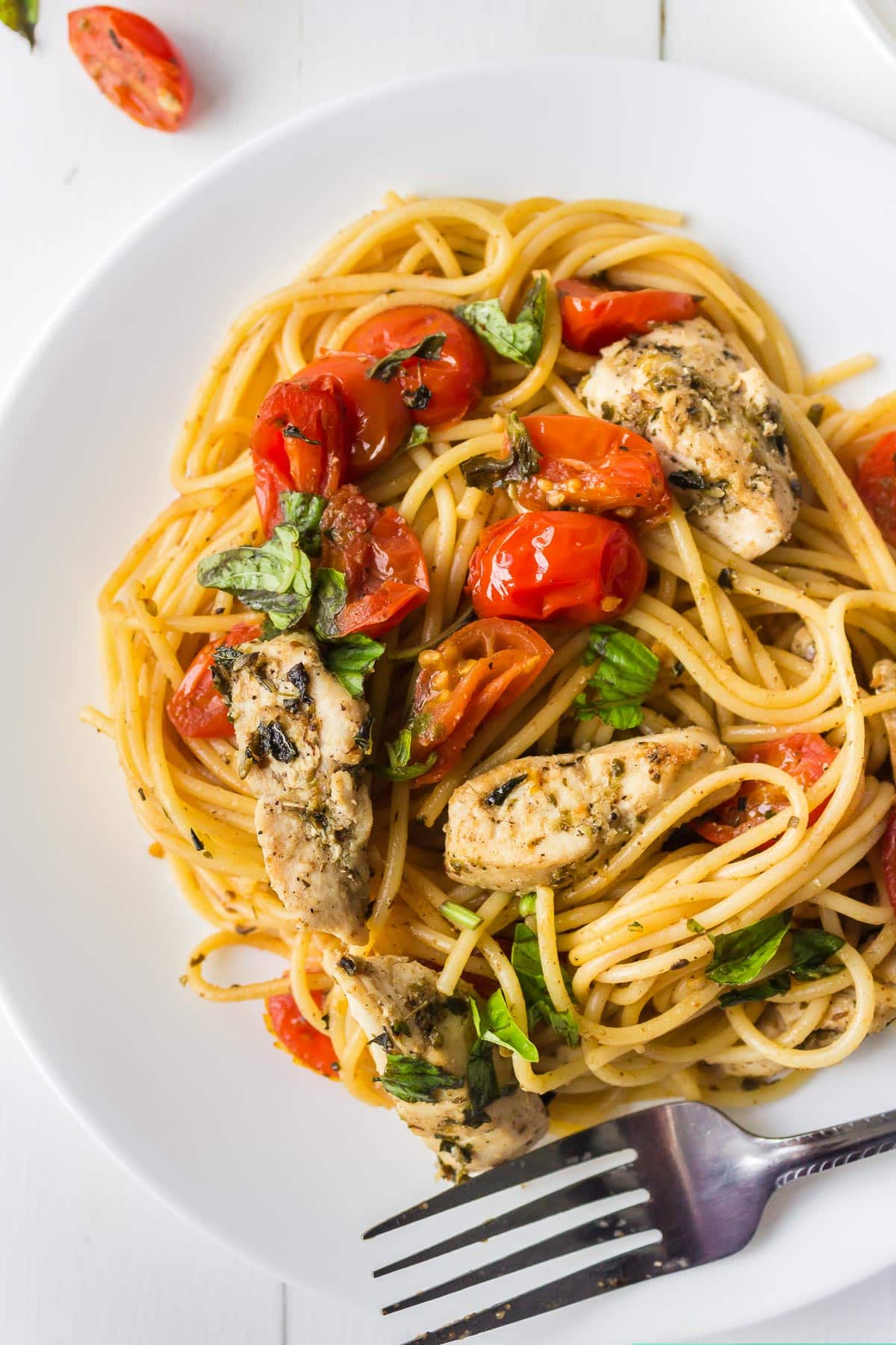A plate of spaghetti with grilled chicken, cherry tomatoes, fresh basil, and a fork on a white table—perfect for those looking for easy pasta recipes and fresh summer flavors.