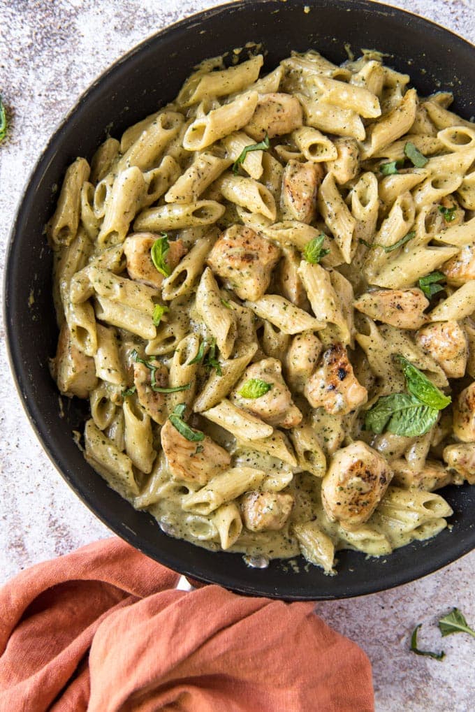 A skillet filled with penne pasta, pieces of cooked chicken, and a creamy pesto sauce, garnished with fresh herbs—perfect for anyone seeking easy summer recipes.