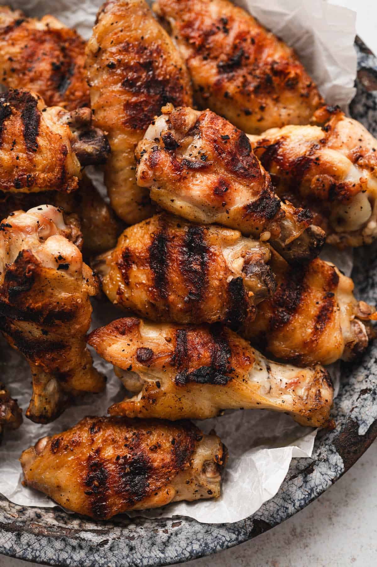 A plate of summer grilled chicken wings with visible grill marks, arranged on parchment paper.