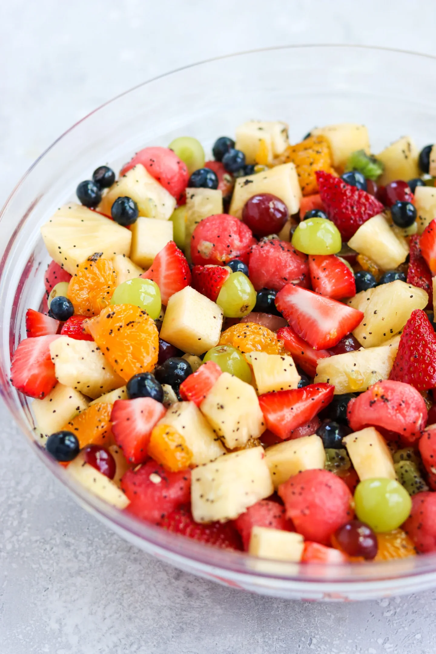 A clear glass bowl filled with a mixed fruit salad—strawberries, pineapple, watermelon, grapes, blueberries, and orange segments—makes a vibrant side dish perfect for any graduation party.