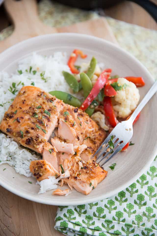 A plate with cooked salmon on white rice, mixed vegetables including red bell pepper and cauliflower, and a fork resting on the plate makes for one of the perfect healthy grilled dinners.
