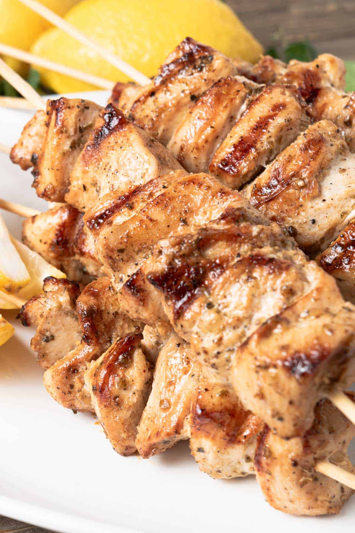 High protein grilled chicken skewers seasoned with herbs and spices on a white plate, perfect for summer, with lemon wedges in the background.