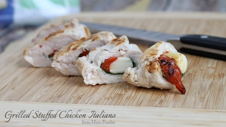 Sliced summer grilled chicken breast stuffed with cheese, spinach, and roasted red pepper sits on a wooden cutting board next to a knife.