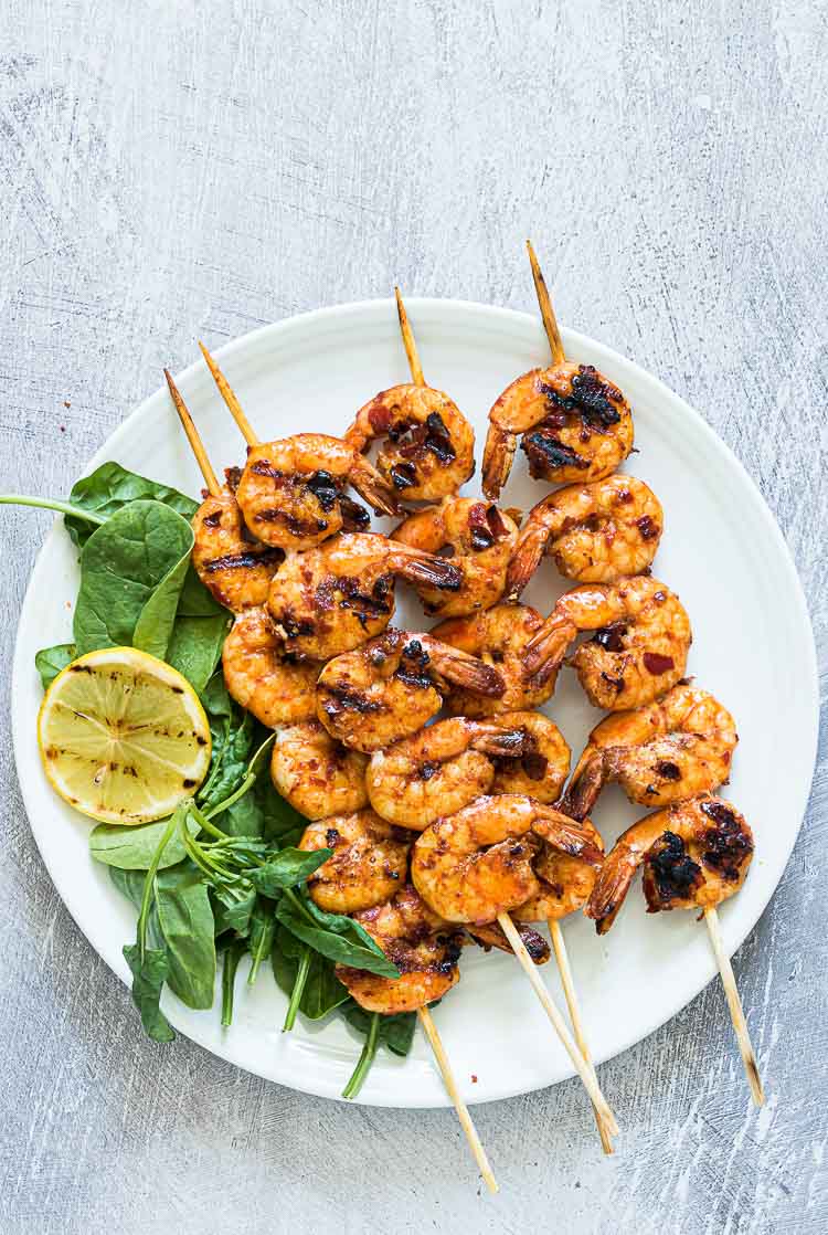 Grilled shrimp skewers served on a white plate with spinach leaves and a grilled lemon slice—perfect for a light summer dinner.