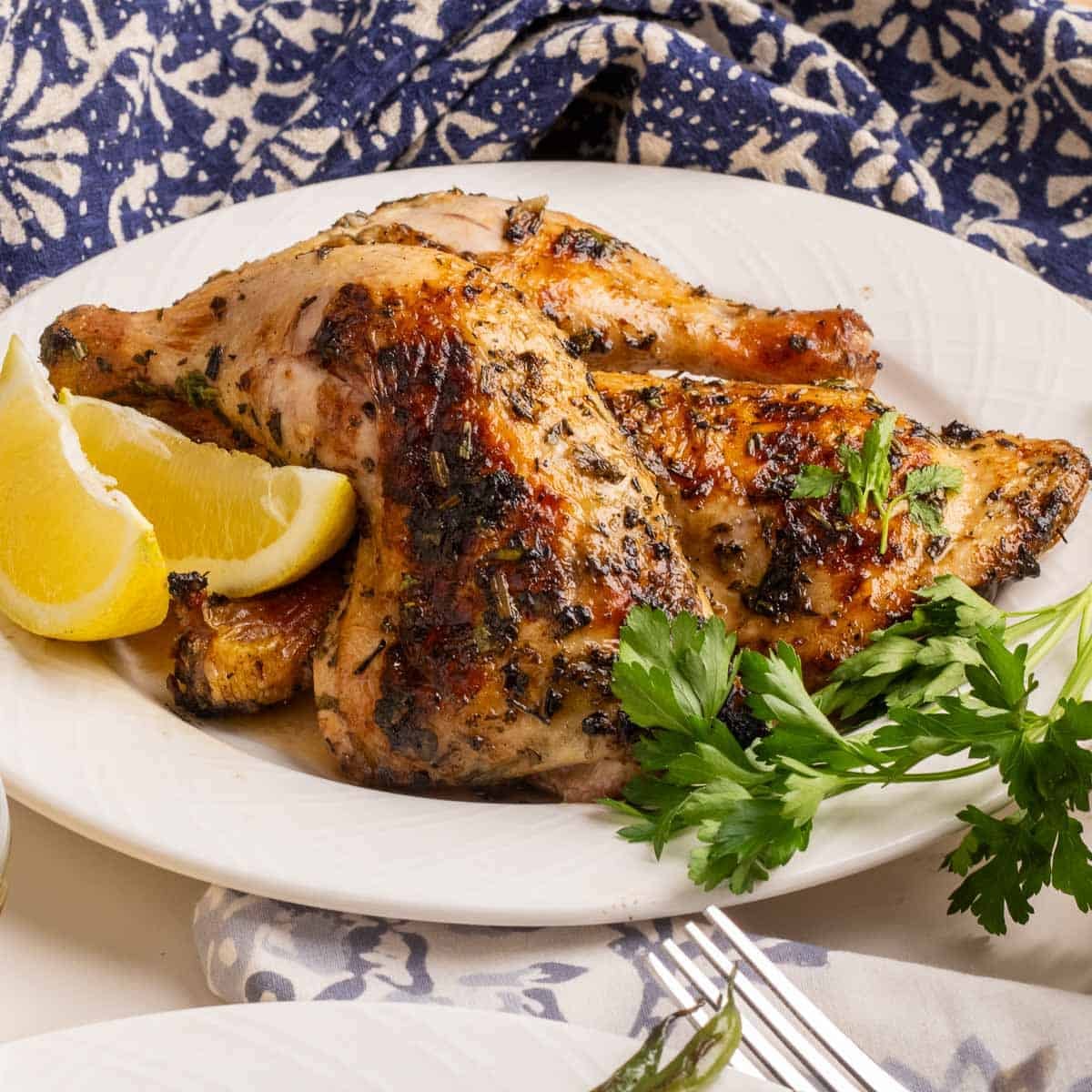 Grilled chicken quarters, perfect for summer grilling, garnished with parsley and lemon wedges on a white plate.