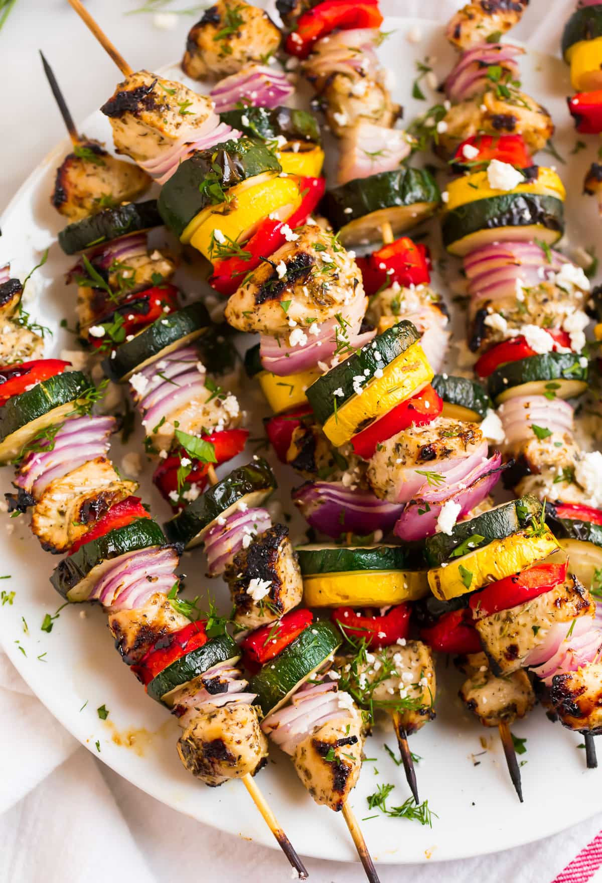 Enjoy healthy grilled dinners with chicken and vegetable skewers featuring zucchini, yellow squash, red onion, and red bell pepper, garnished with herbs and feta cheese on a white plate.