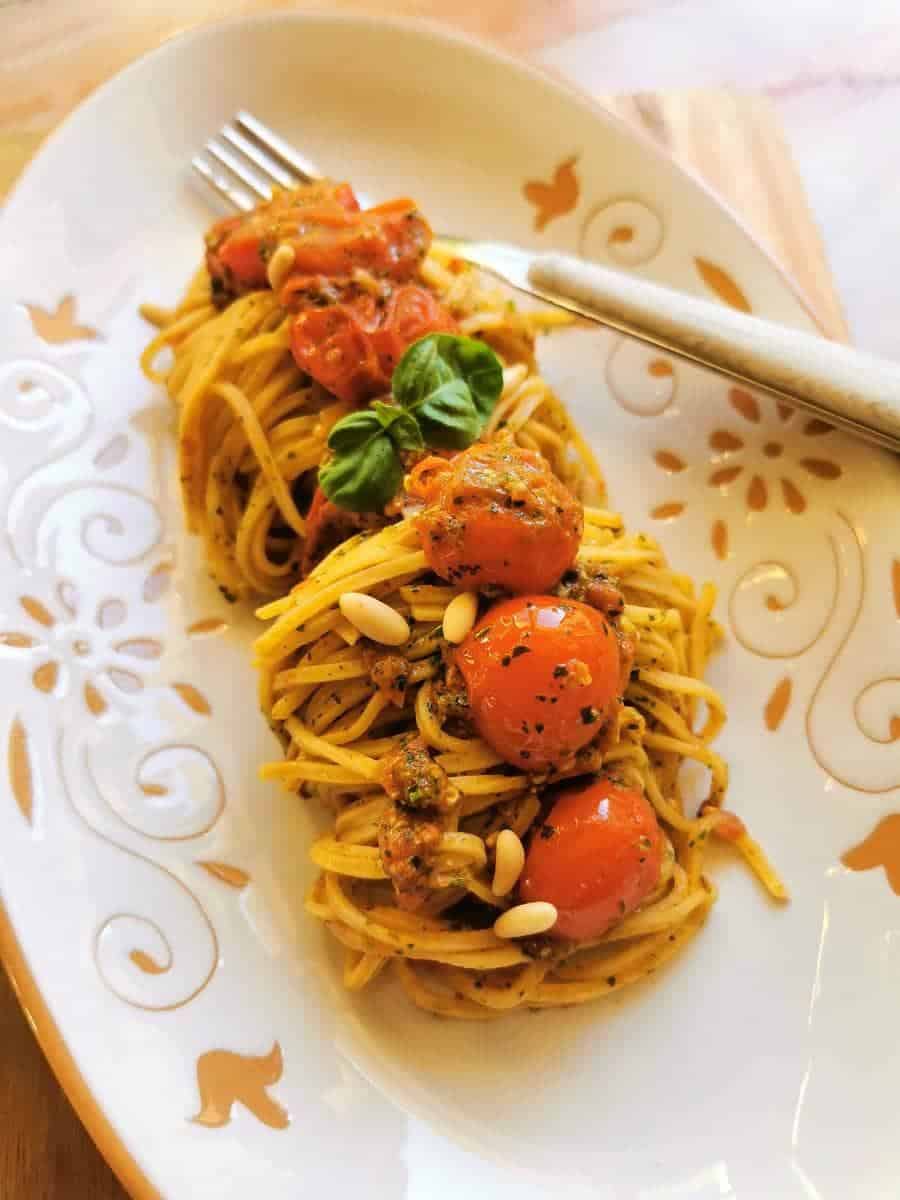 A plate of spaghetti topped with cherry tomatoes, pesto, pine nuts, and a basil garnish, served with a fork on a decorative white dish—perfect for Italian Summer Recipes.
