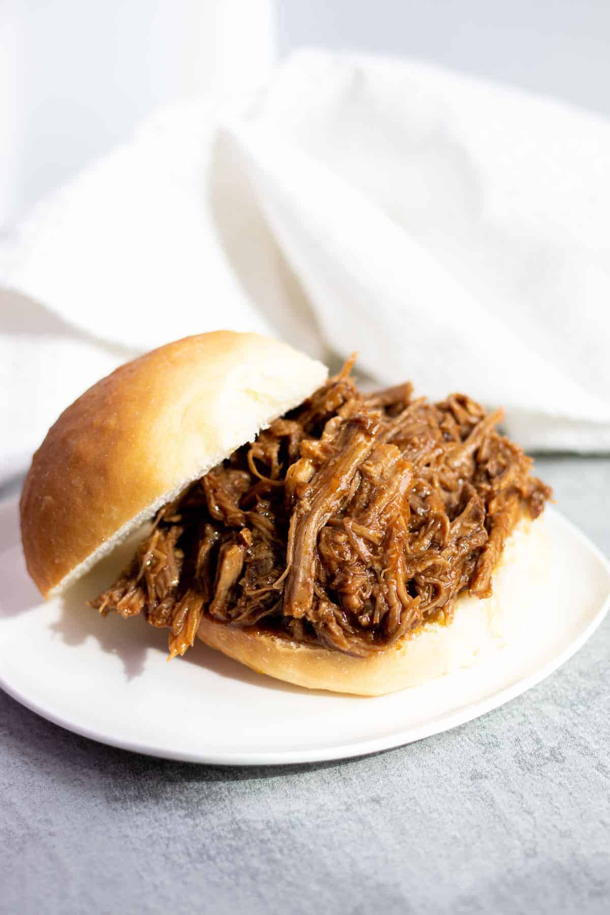 A shredded barbecue beef sandwich, perfect for summer recipes, served on a white plate with a white napkin in the background.