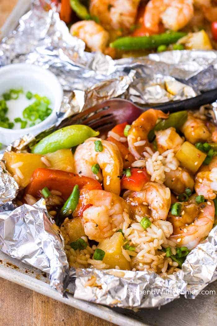 Shrimp, rice, vegetables, and pineapple chunks served in a foil packet for a healthy grilled dinner, garnished with chopped green onions, with a small dish of green onions on the side. Perfect for those who love healthy grilling.