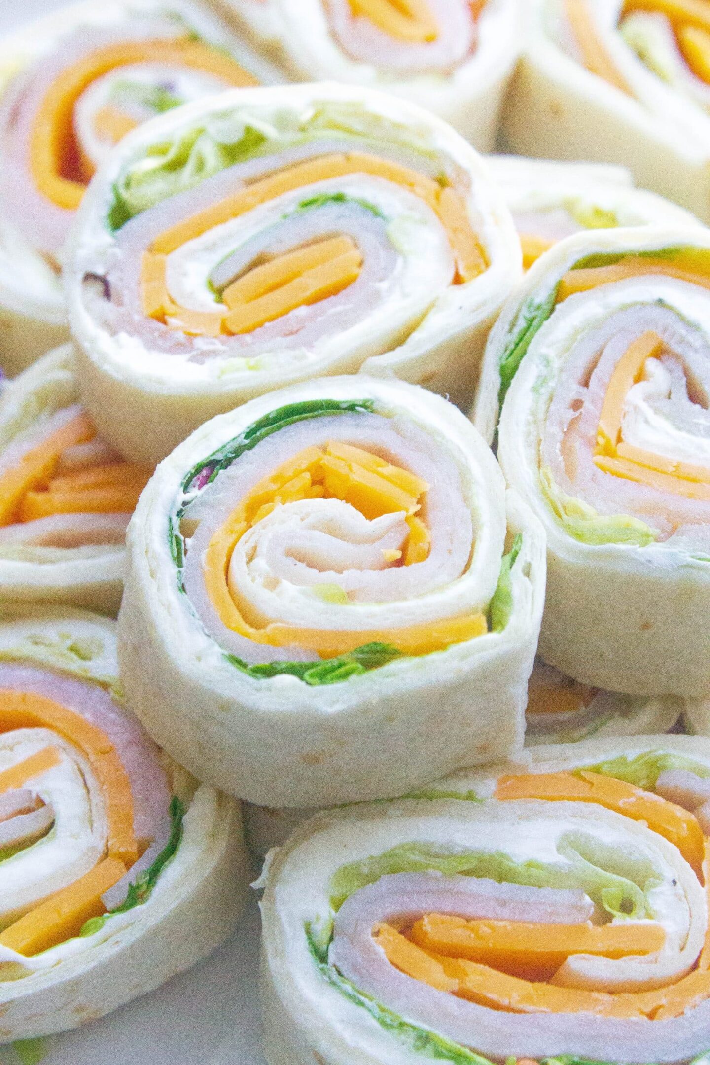 Close-up of several tortilla pinwheel sandwiches filled with sliced turkey, cheddar cheese, lettuce, and cream cheese—perfect for cold beach lunch ideas.