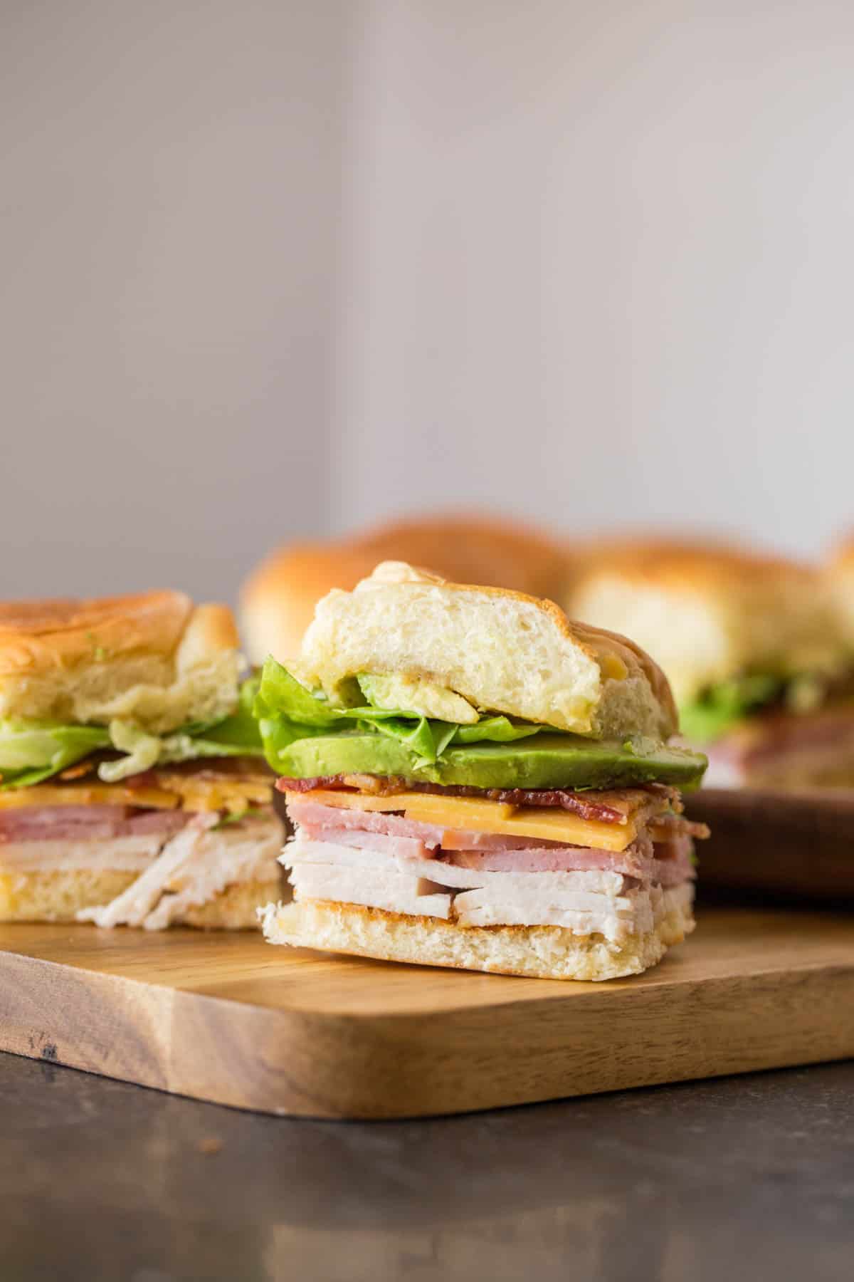 A close-up of a sandwich with layers of ham, turkey, cheese, lettuce, and tomato on a wooden cutting board—perfect for kids lunch or as one of your easy pool lunch ideas.