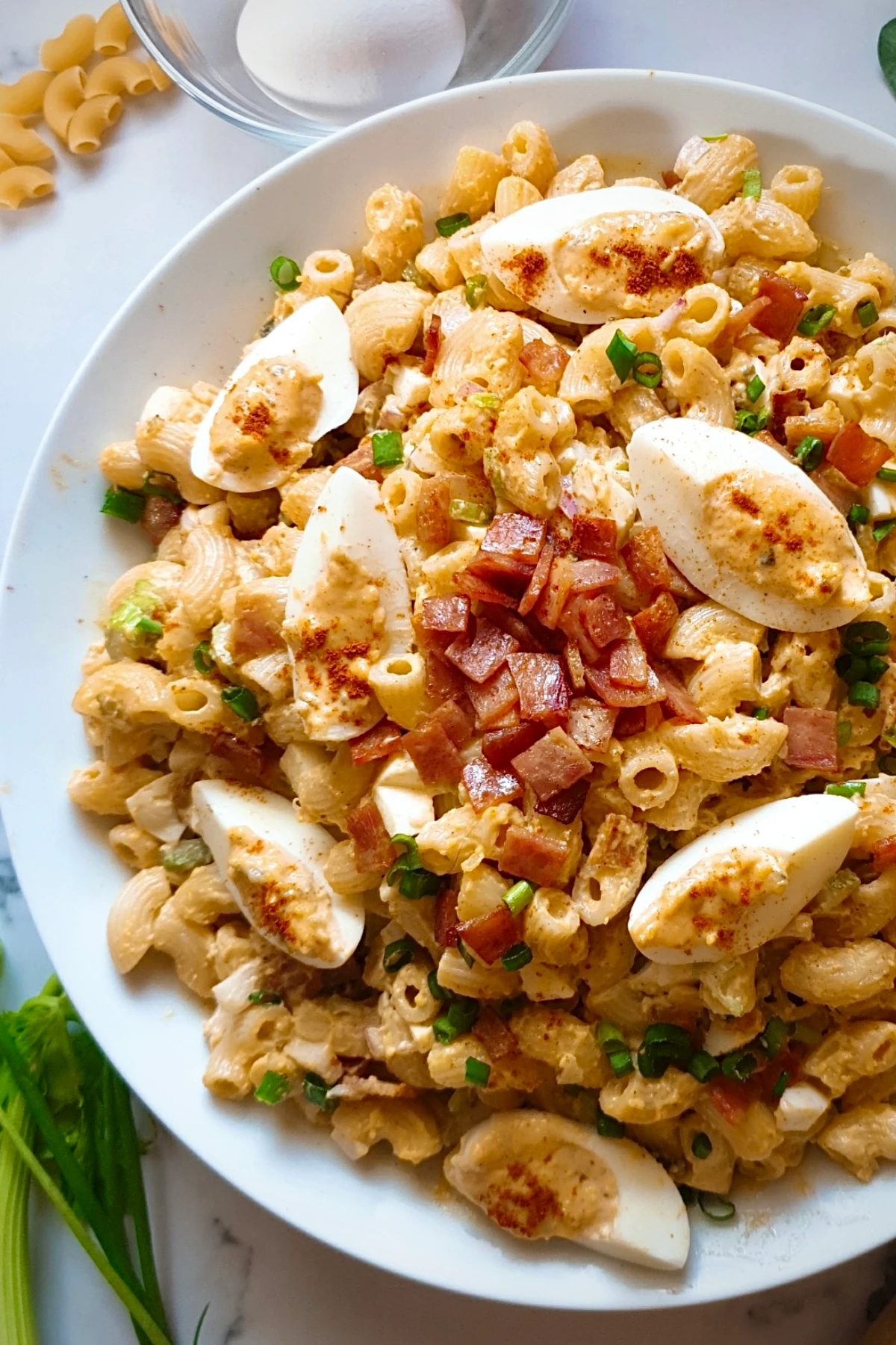 A bowl of macaroni salad topped with sliced boiled eggs, diced ham, chopped green onions, and a sprinkle of paprika—perfect for side dishes at your next graduation party.