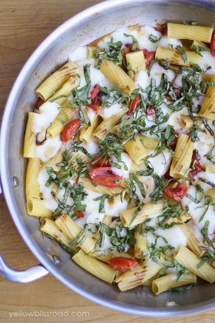 Cooked rigatoni pasta in a skillet with melted mozzarella, cherry tomatoes, and fresh chopped basil on top—perfect for easy summer recipes or quick summer pasta recipes.