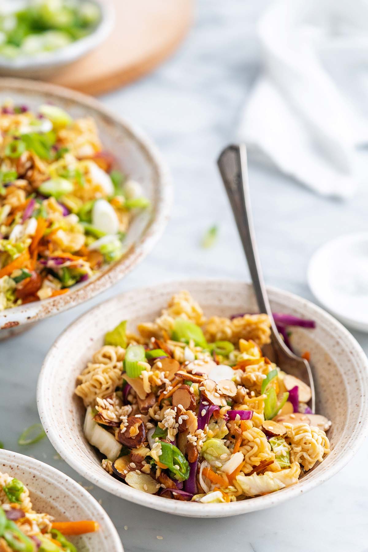 A bowl of Asian-inspired salad with chopped vegetables, crunchy noodles, sesame seeds, and green onions makes a vibrant choice for side dishes at your graduation party, with a fork resting in the bowl.