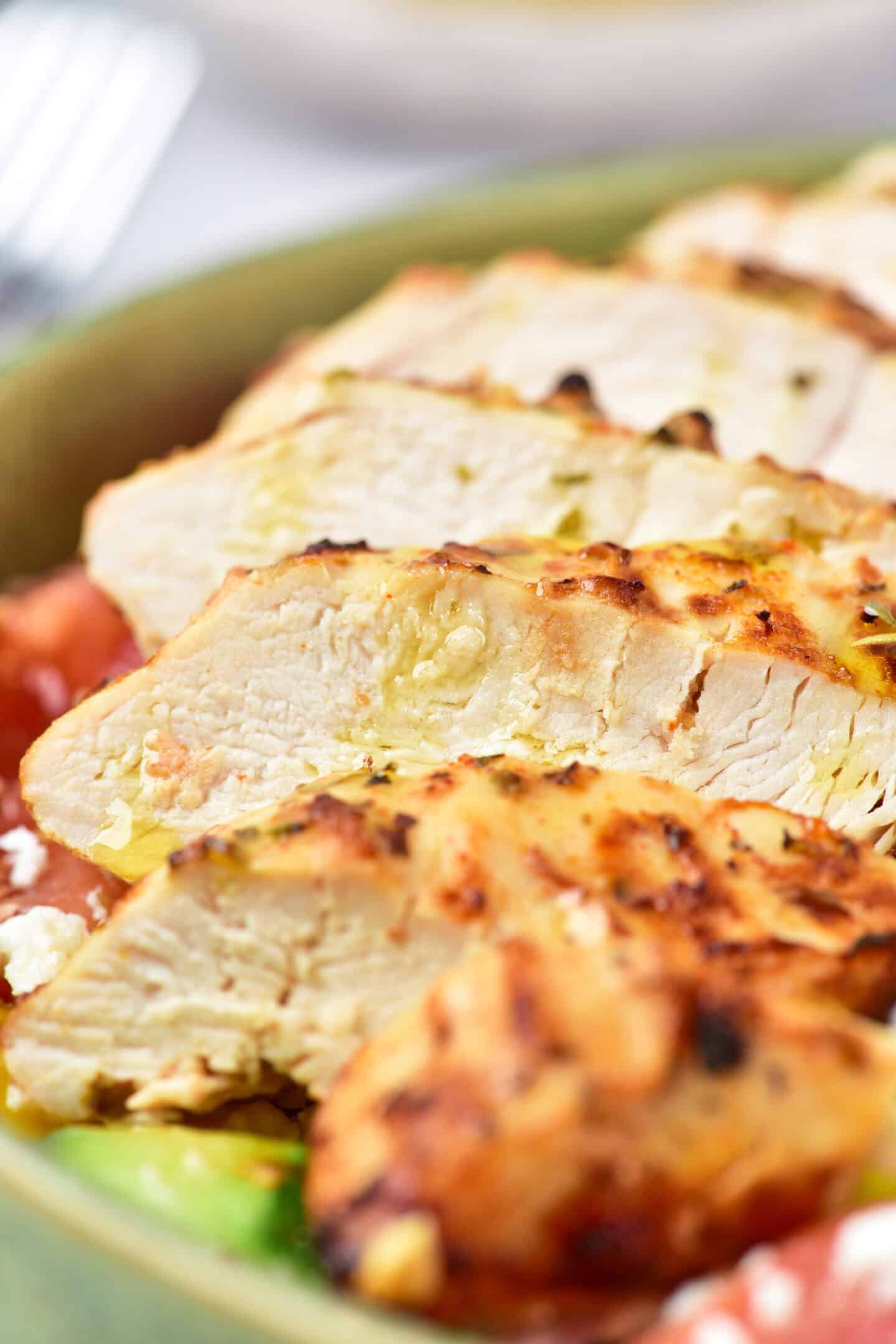 Sliced Greek chicken breast arranged over a bed of vegetables creates delicious and healthy chicken bowls.