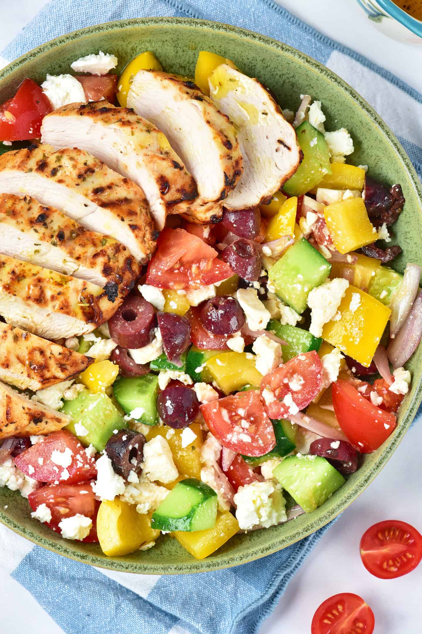 A bowl of Greek salad with chopped tomatoes, cucumbers, bell peppers, olives, feta cheese, red onion, and sliced Air Fryer Greek Chicken breast on top.