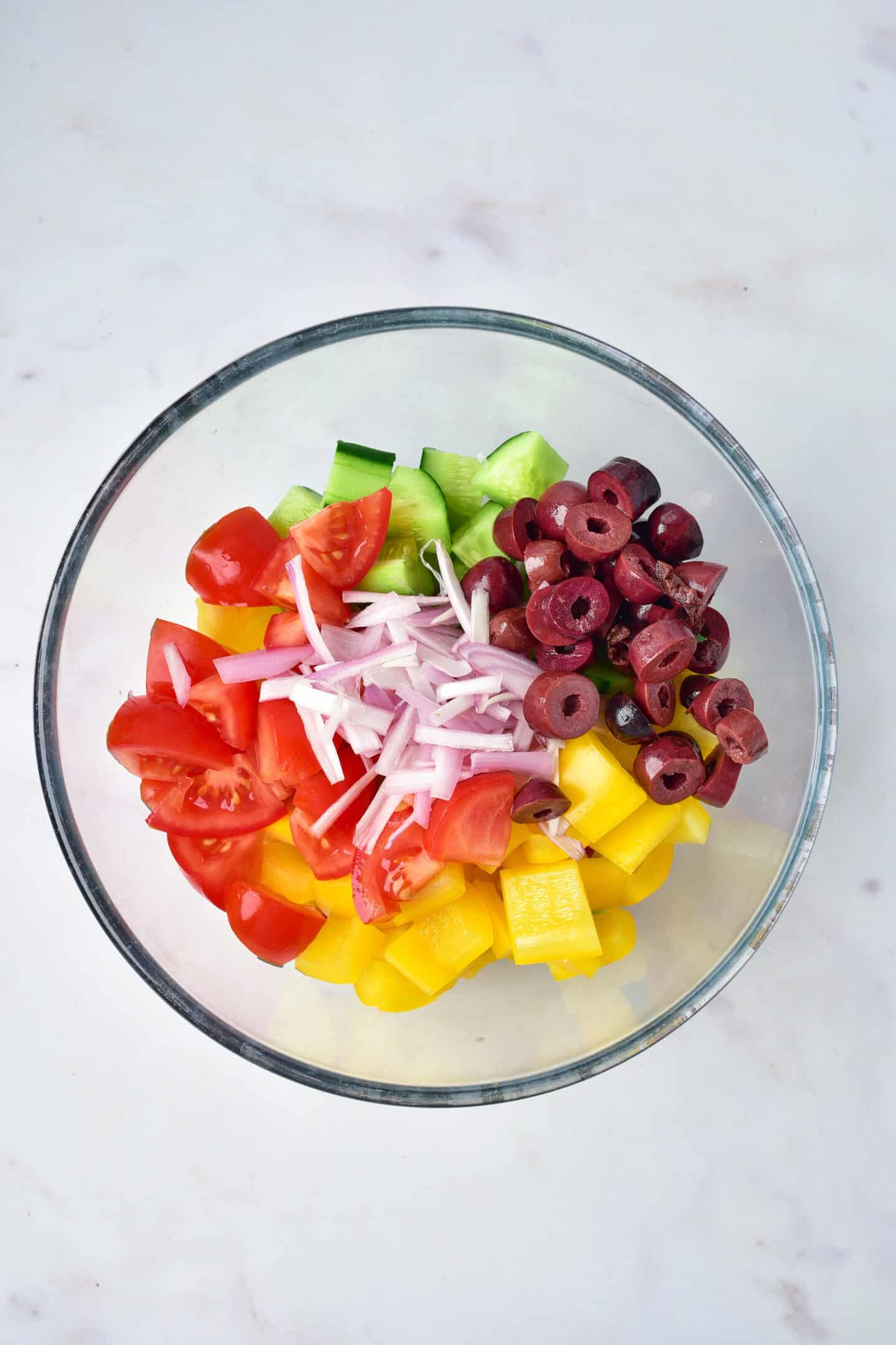 A glass bowl containing chopped tomatoes, cucumber, yellow bell pepper, red onion, and sliced black olives—perfect toppings for Greek Chicken bowls or a fresh side for your favorite Air Fryer meals.
